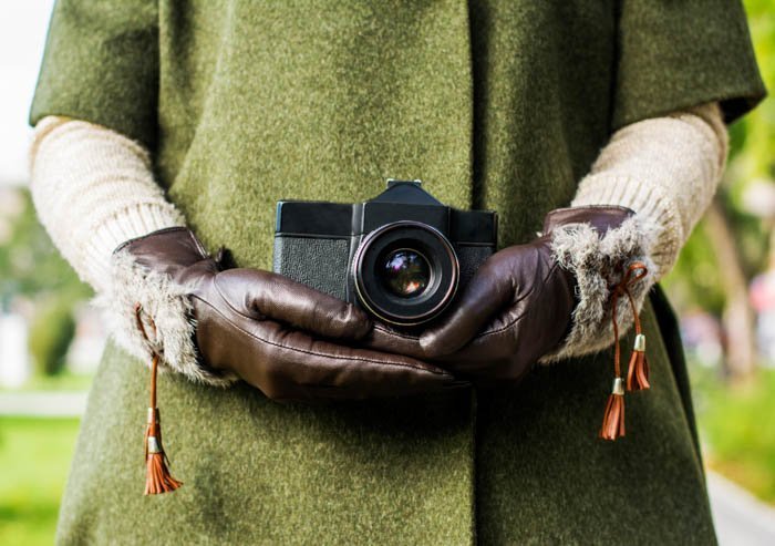 Hands in leather photography gloves holding a camera
