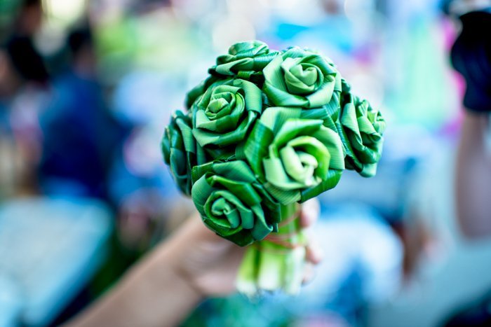 Close up of a hand holding a bunch of green handmade craft flowers, blurry background. Documentary photography.